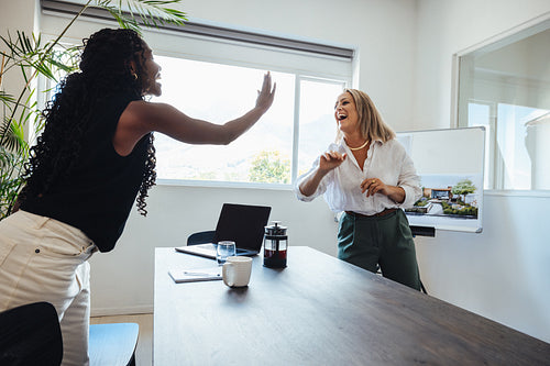 Two female professionals celebrating a milestone in a creative office setting