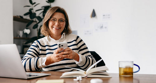 Smiling woman texting with smartphone at her home office desk