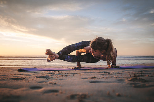 Woman doing Ashtavakrasana yoga at beach