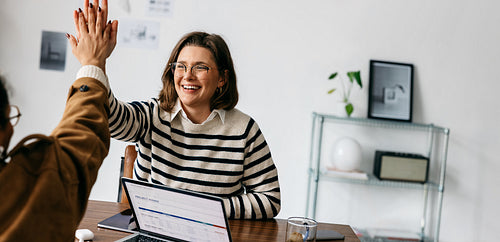 Business people celebrate success with high five during office meeting at laptop desk