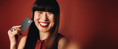 The woman presents a bank card with a smiling look in the studio