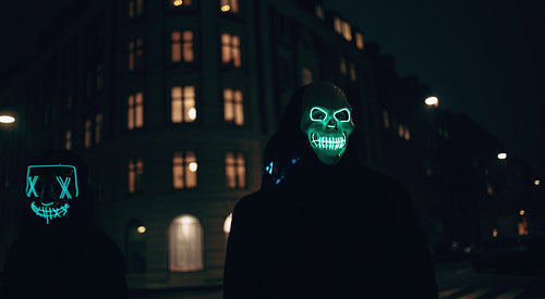 Two individuals wearing glowing masks on an urban street at night