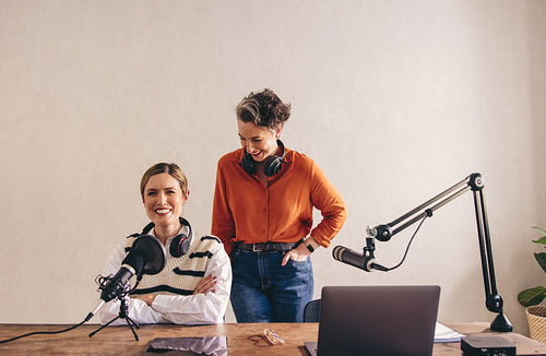 Cheerful female podcasters laughing together in a home studio