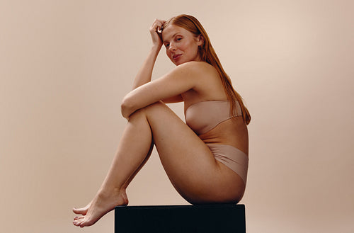 Content woman in nude underwear seated in studio