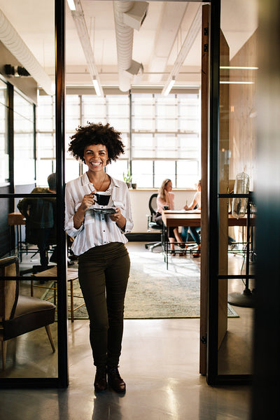 Smiling woman standing in office doorway with coffee
