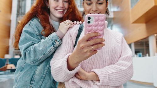 College girls using a smartphone together, engaging with social media after class