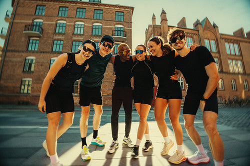 Together after the run, running friends pose outdoors in an urban club scene