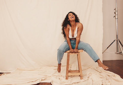 Woman laughing cheerfully while sitting on a chair in a studio