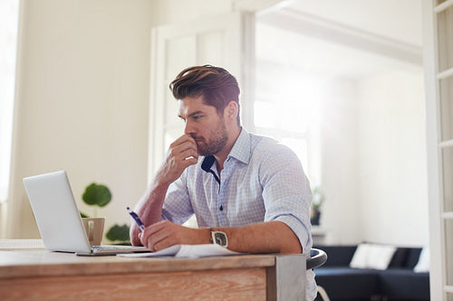 Pensive young man working on laptop at home