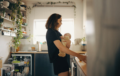 Tired mother holding crying baby while trying to make breakfast