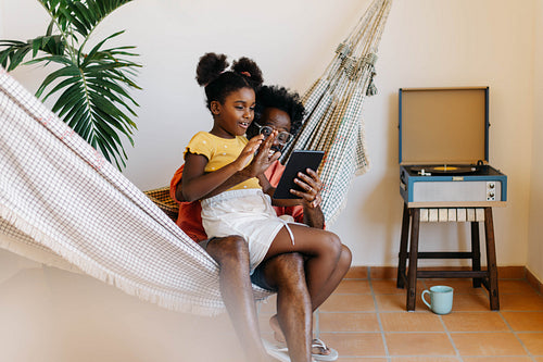 Video call in a hammock: Dad and daughter using a tablet together at home