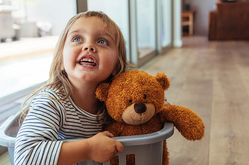 Girl sitting in washing basket with her teddy