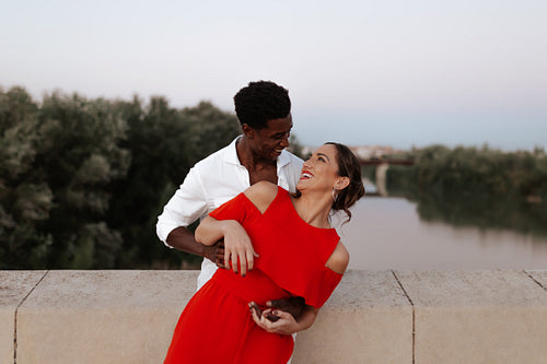 Interracial couple laughing happily on a bridge