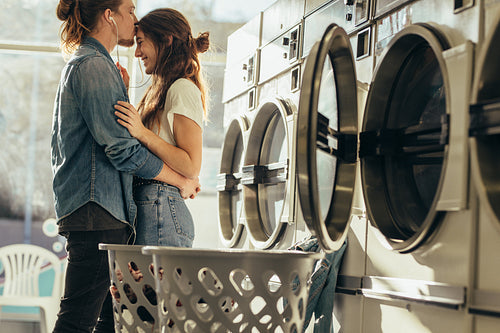 Man kissing his girlfriend on forehead standing in a laundry room