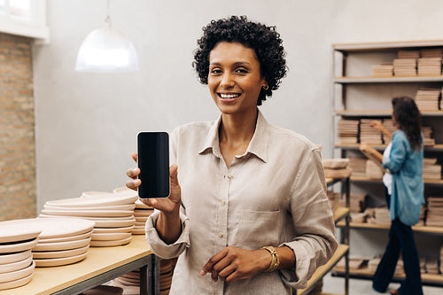 Happy ceramic shop owner showing a blank smartphone screen
