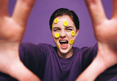 Young woman taking a selfie with smiley stickers on her face