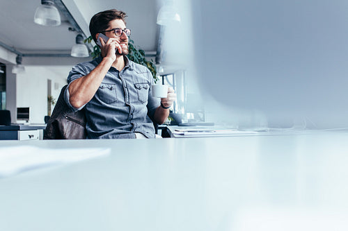 Young man with cup of coffee and talking on cellphone