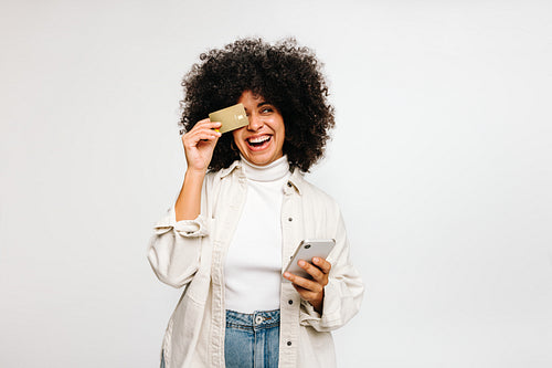 Cheerful young woman holding a credit card and a smartphone in a studio