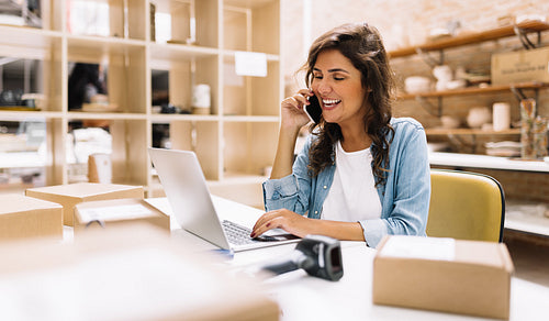 Happy female entrepreneur speaking on the phone in a warehouse