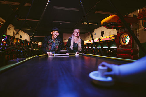 Smiling young friends playing air hockey game