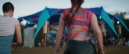 Two young women run towards festival stage at sunset