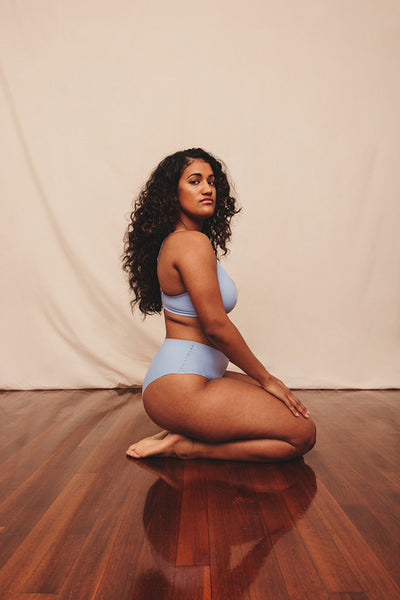 Young woman kneeling while wearing blue underwear in a studio
