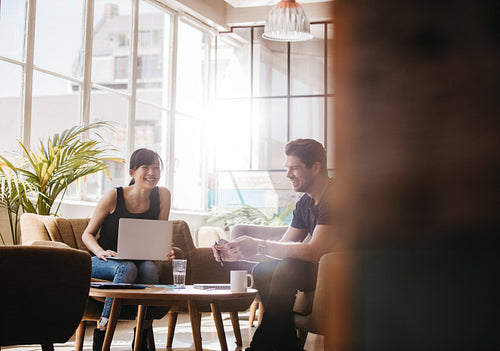 Two businesspeople sitting in office lobby talking and smiling