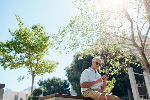 Senior man sitting outdoors and using cell phone