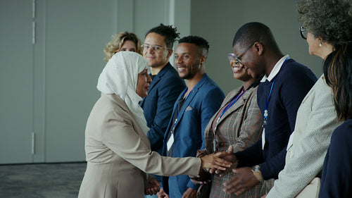 A businesswoman wearing a hijab shaking hands with a diverse group of professionals