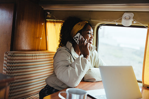 Girl in a van talking on the phone with laptop nearby