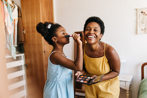 Young daughter doing her mother's makeup with a brush