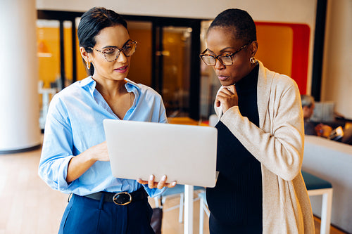 Two professionals discussing work while looking at a laptop in the office