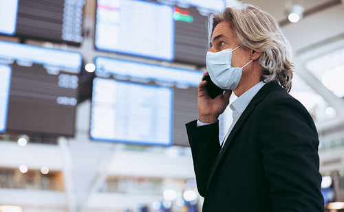 Man with face mask at airport terminal talking on phone
