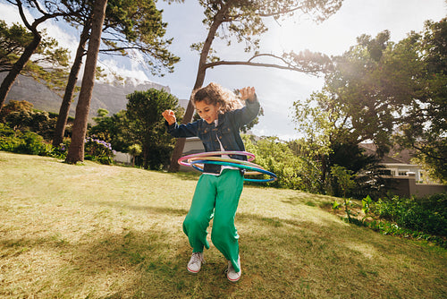 Girl hula hooping in a sunny backyard surrounded by lush greenery