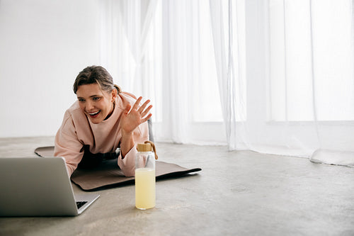 Woman using laptop on yoga mat for online fitness session at home
