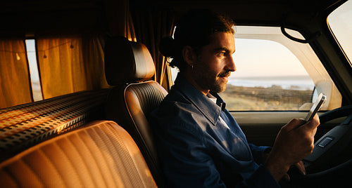 Man scrolls his phone while driving a van at sunset