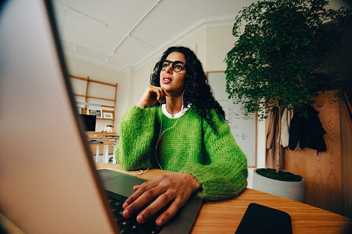 Woman working on laptop at office desk with headphones in a bright workspace