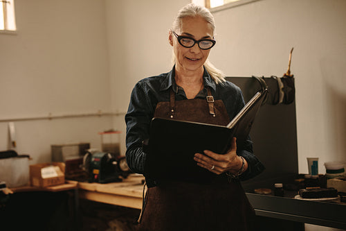 Smiling jewelry designer with design book at workshop