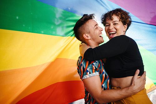 Happy queer couple standing against rainbow flag