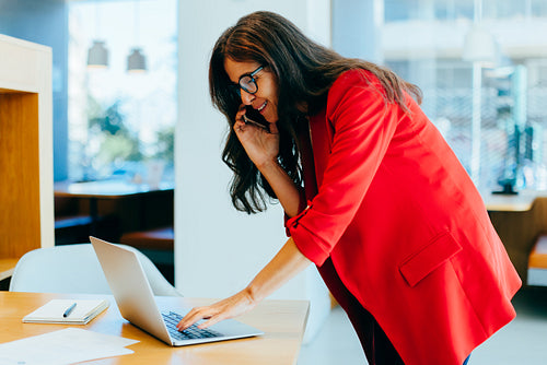 Businesswoman multitasking with a phone call and laptop in an office setting