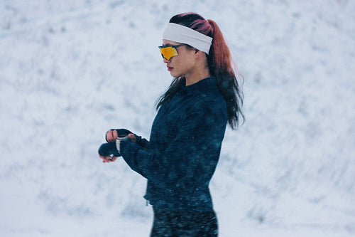Woman in a snowy outdoor setting checks her watch during winter running training