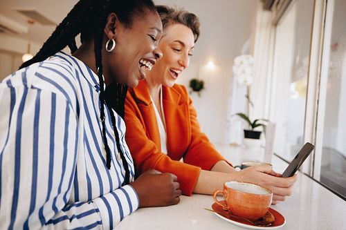 Two business women video calling their team on a smartphone in a coffee shop