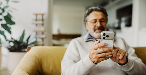 Senior checks a smartphone on a sofa at home