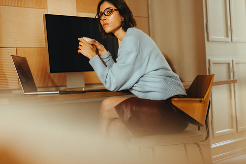 Pensive woman holds coffee during desk work with a laptop