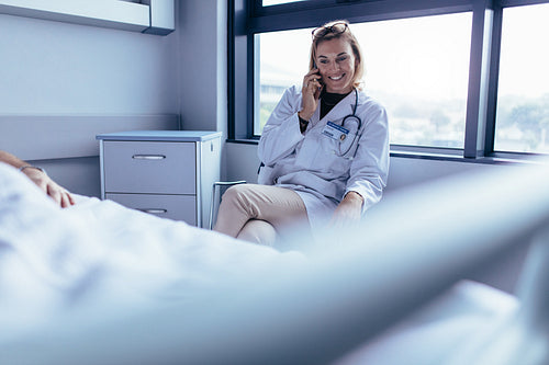 Doctor sitting in hospital ward and talking on mobile phone