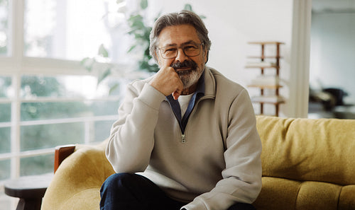 Senior man poses on a sofa in a warm home