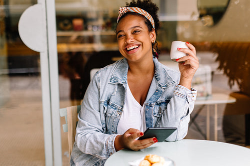 Happy young woman enjoying a cup of coffee at a cafe while using a digital tablet