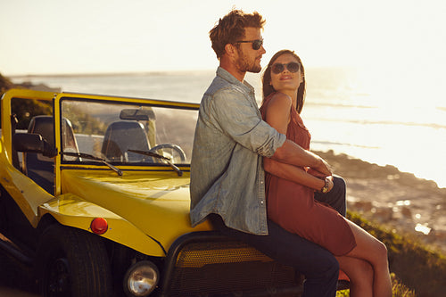 Romantic young couple sitting on the hood of their car