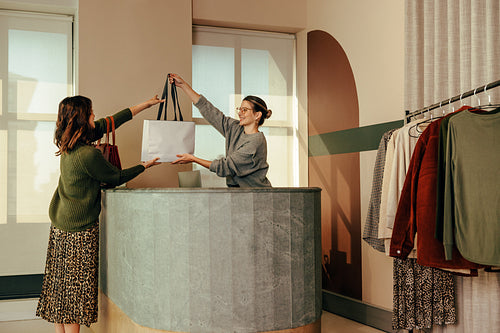 Cheerful clothing store owner assisting a female customer