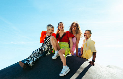 Friends laugh together while sitting outdoors under a clear blue sky